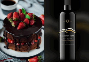 A rich chocolate cake layered with strawberries and glossy ganache, pictured beside a bottle of Elkhorn Peak red wine.