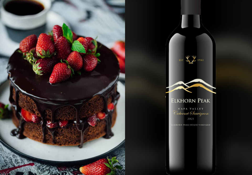 A rich chocolate cake layered with strawberries and glossy ganache, pictured beside a bottle of Elkhorn Peak red wine.