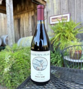 Elkhorn Peak Pinot Noir bottle placed on a black metal table outside a rustic winery building.