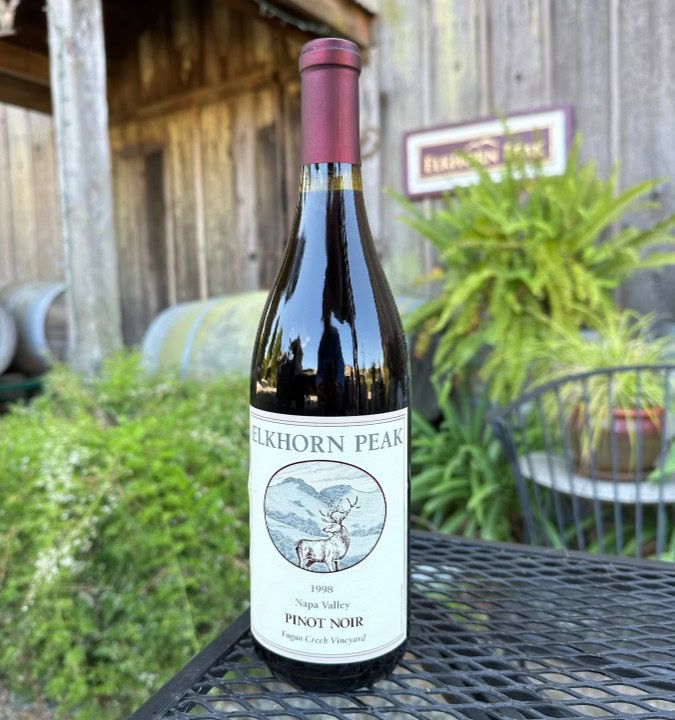 Elkhorn Peak Pinot Noir bottle placed on a black metal table outside a rustic winery building.