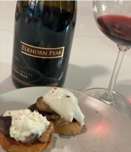 Two mushroom crostini with cheese served alongside a bottle of Elkhorn Peak Pinot Noir and a glass partially filled.