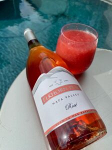 Bottle of Elkhorn Peak Napa Valley Rosé resting on a white surface next to a chilled glass with a frosé, positioned beside a blue swimming pool.