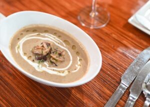 Bowl of creamy mushroom soup garnished with sautéed mushrooms and a swirl of cream, on a wooden table.